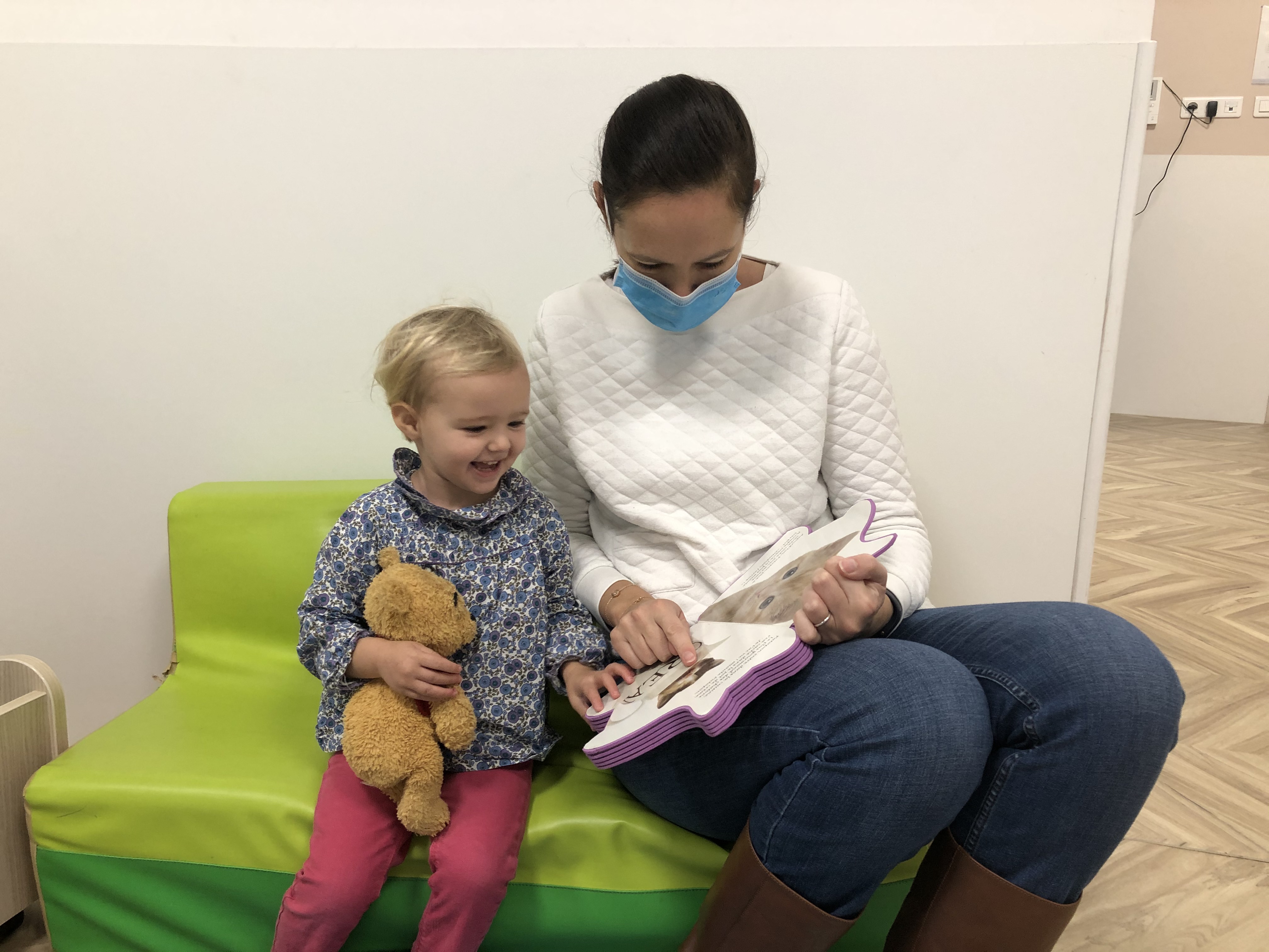 dans une crèche une pro masquée lit un livre à une petite fille